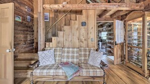 L’intérieur d’une cabane en rondins, avec un canapé à carreaux, un escalier en bois et une vitrine contenant divers objets.