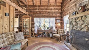 L’intérieur d’une cabane en rondins, avec un plafond en bois, une cheminée en pierre, un canapé à carreaux et une radio d’époque.