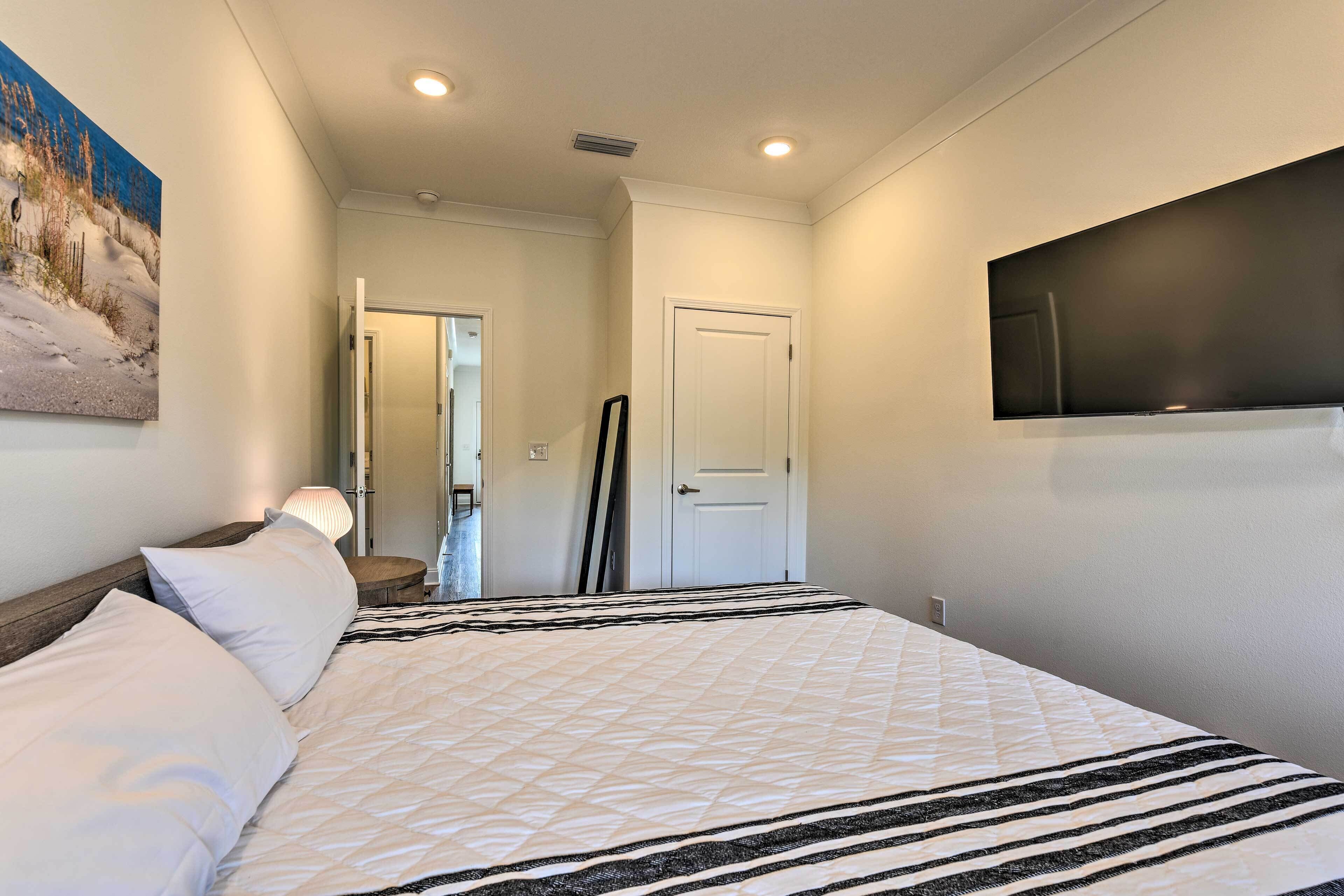 Habitación de hotel con cama, un cuadro en la pared, televisor montado y una puerta que da a otra habitación.
