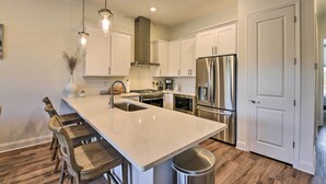 A modern kitchen with white cabinets, stainless steel appliances, and a large island with bar stools. - Santa Rosa Beach Vacation Rental Near Ocean! (Santa Rosa Beach)