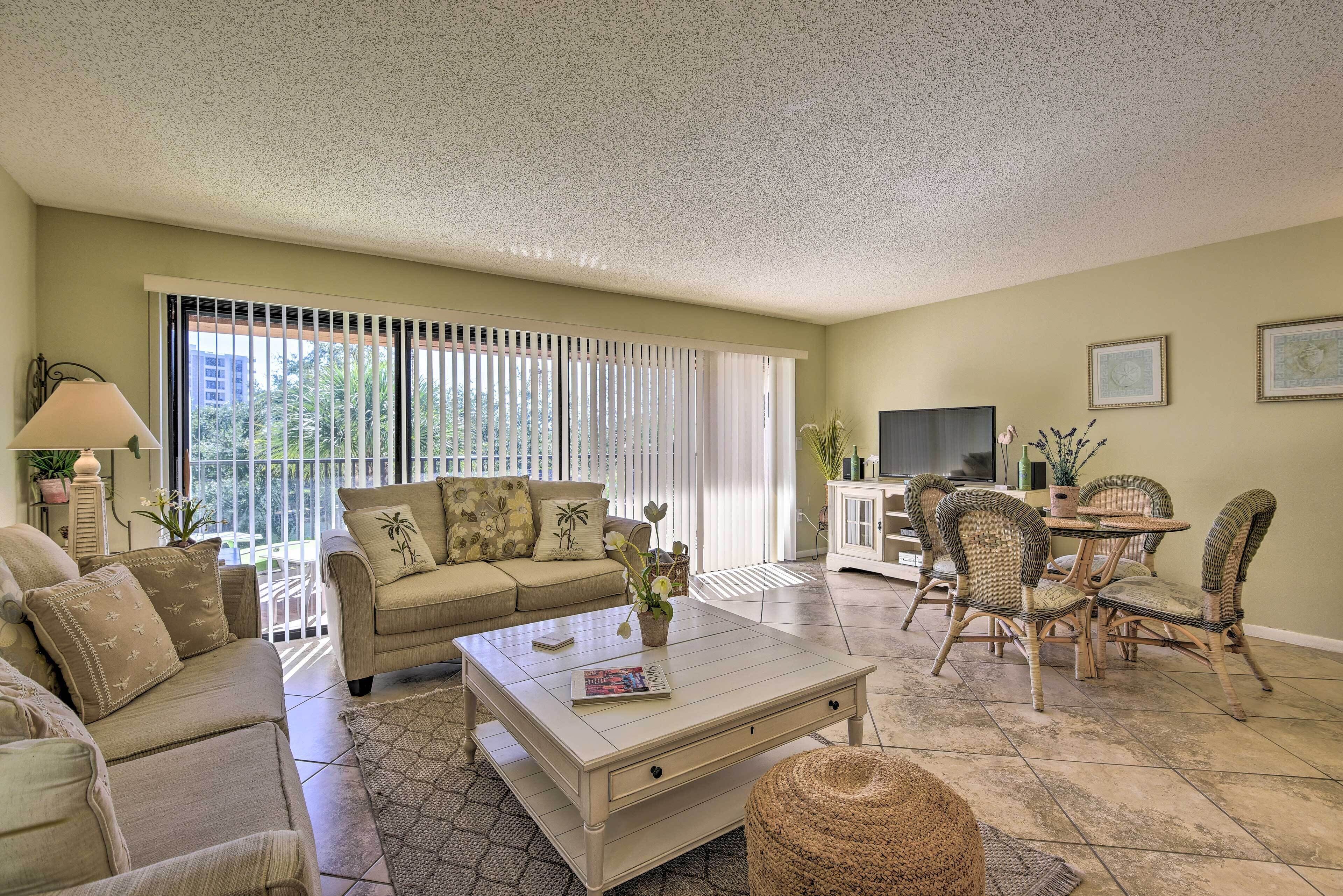 A living room with a beige sofa, a coffee table, wicker chairs, and a dining table.