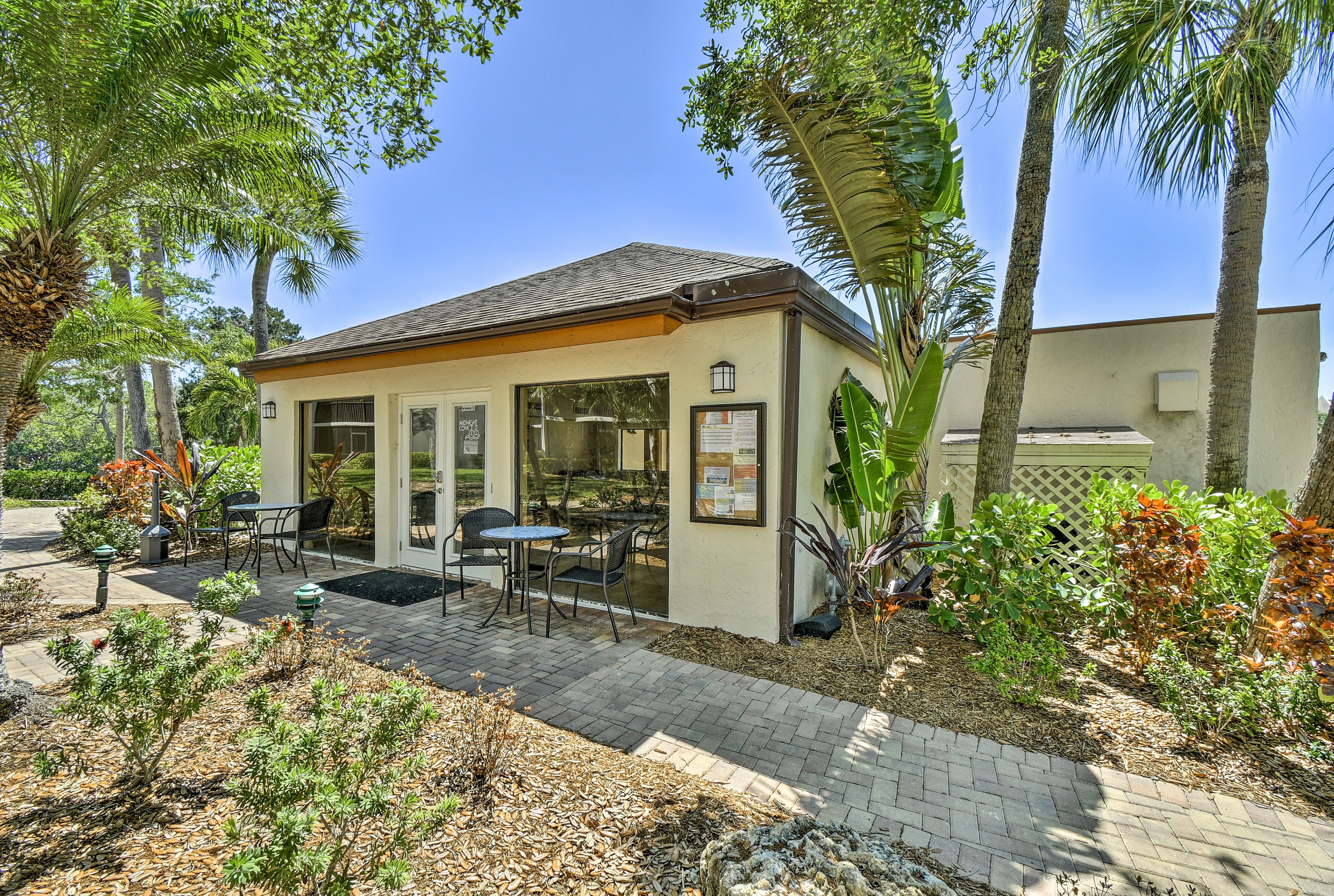 A small building with a patio area, outdoor seating, and a garden with various plants and trees.