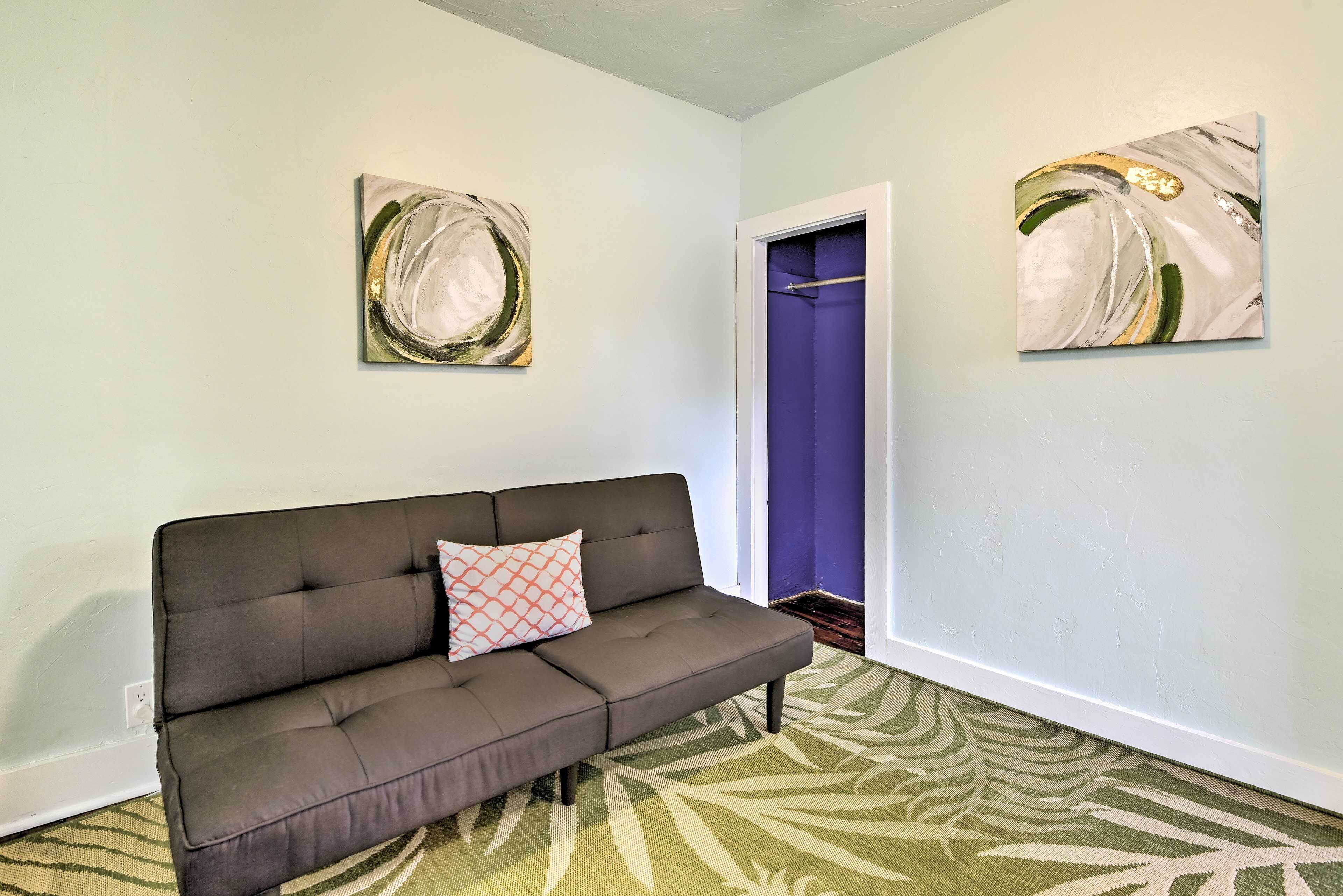 A room with a grey sofa, a patterned rug, and two abstract paintings on the walls.
