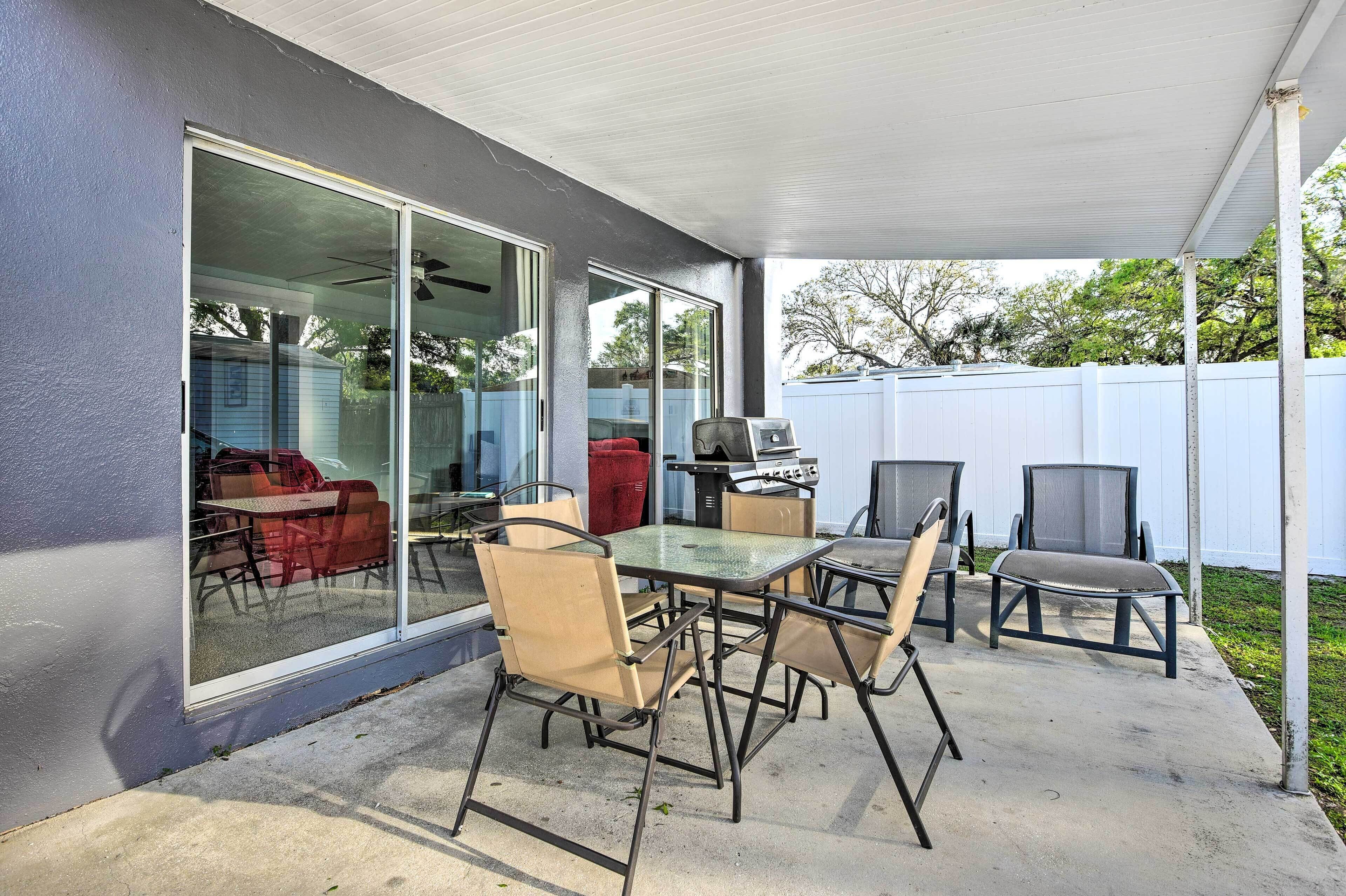 Une terrasse extérieure avec une table et des chaises, une porte-fenêtre coulissante et une clôture blanche en arrière-plan.