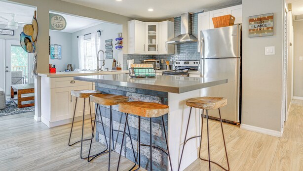 A modern kitchen with white cabinets, a stainless steel refrigerator, and a bar area with stools. - Private & Picturesque Escape on Lake Henry! (Lake Placid)