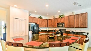 A modern kitchen with wooden cabinets, a central island with seating, and built-in appliances. - Home w/ Private Pool & Spa: 8 Mi to Disney (Kissimmee)