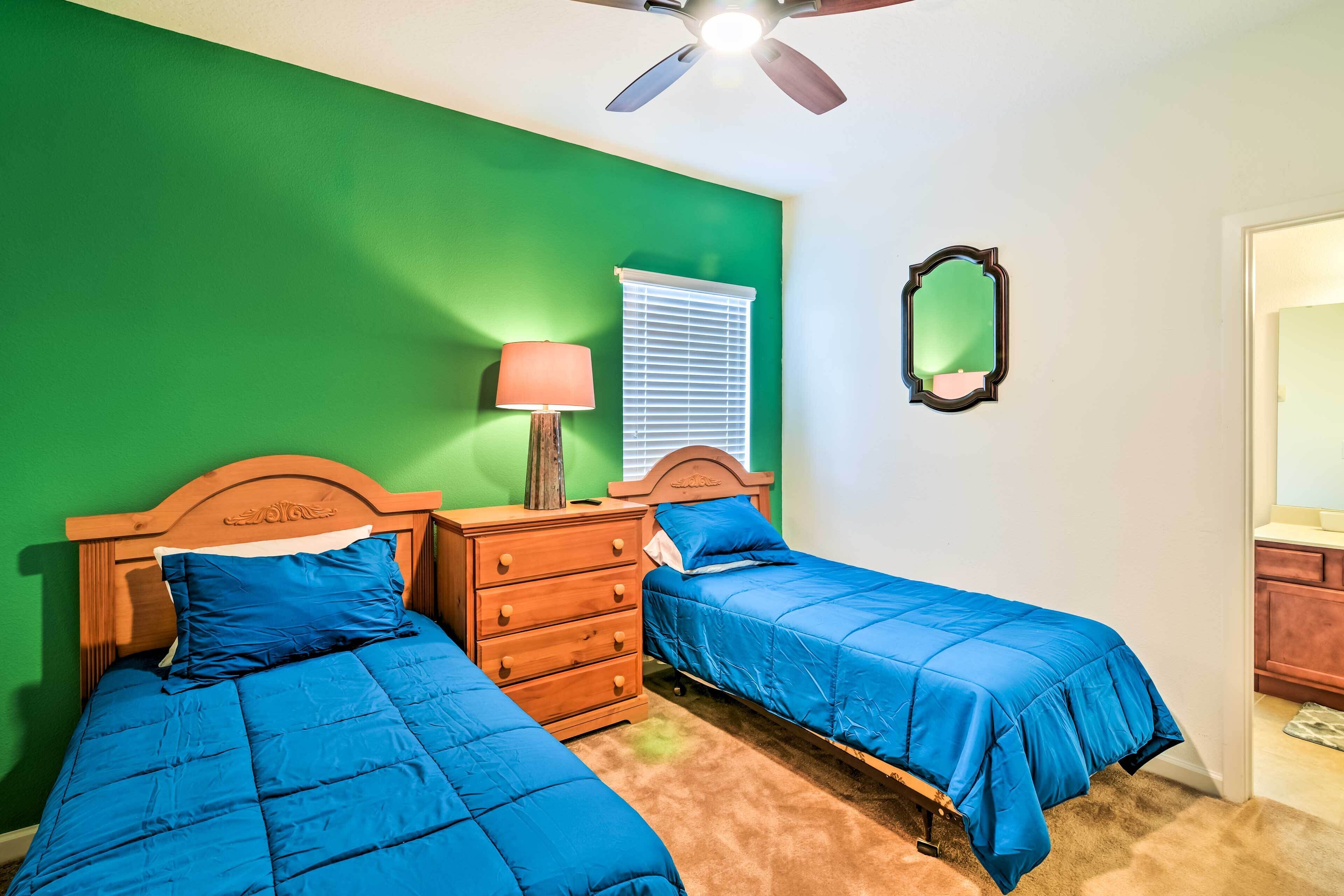 Une chambre avec deux lits, une commode en bois, une lampe et un ventilateur de plafond.