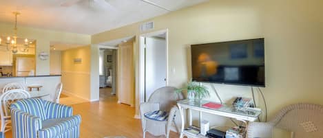 A living room with a flat-screen TV, wicker furniture, a ceiling fan, and a dining area with a white table and chairs.