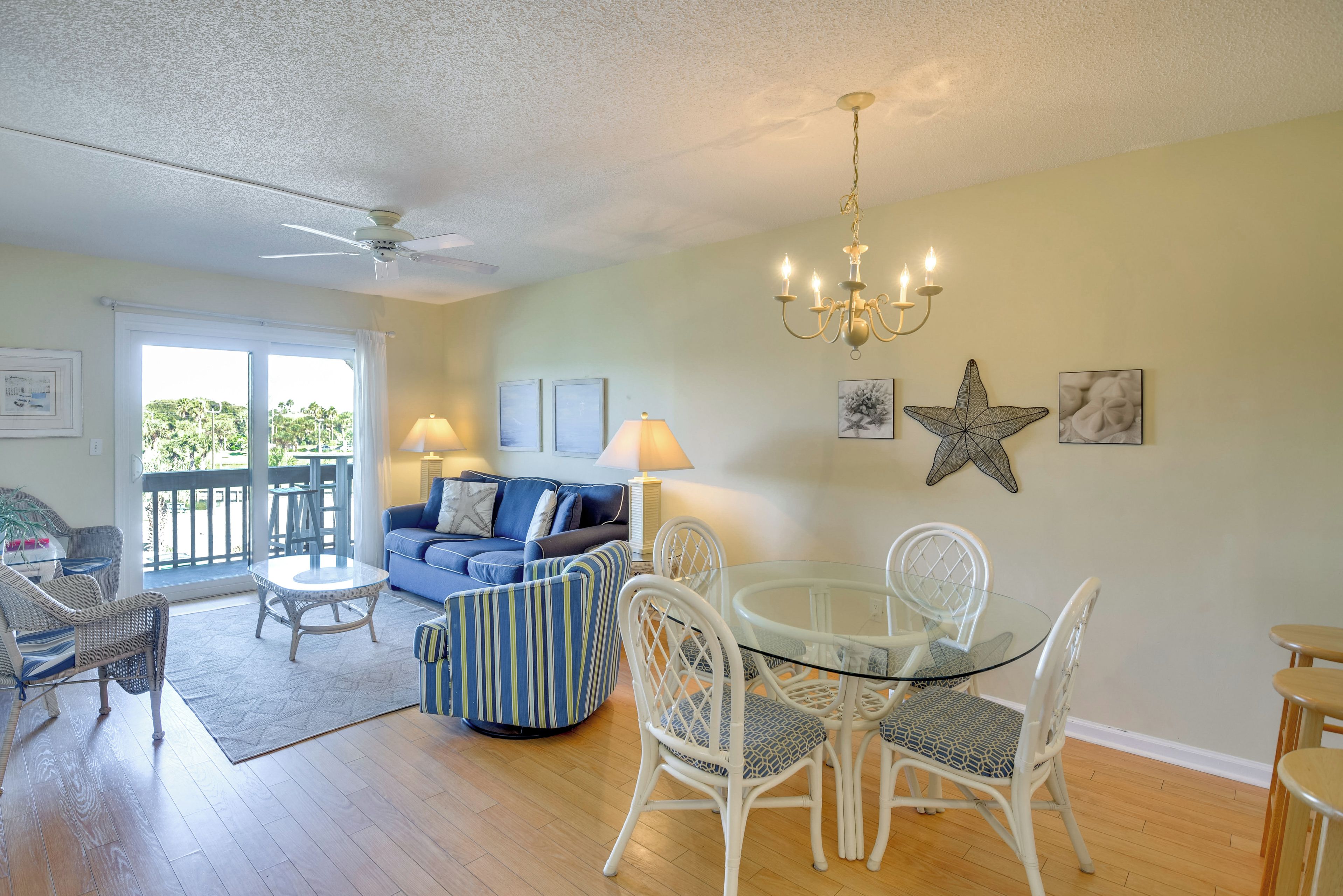 A spacious living area with a balcony, a dining table with chairs, a sofa, and a ceiling fan.