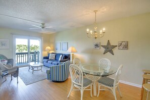 Un vaste espace de vie avec balcon, une table à manger avec des chaises, un canapé et un ventilateur de plafond.