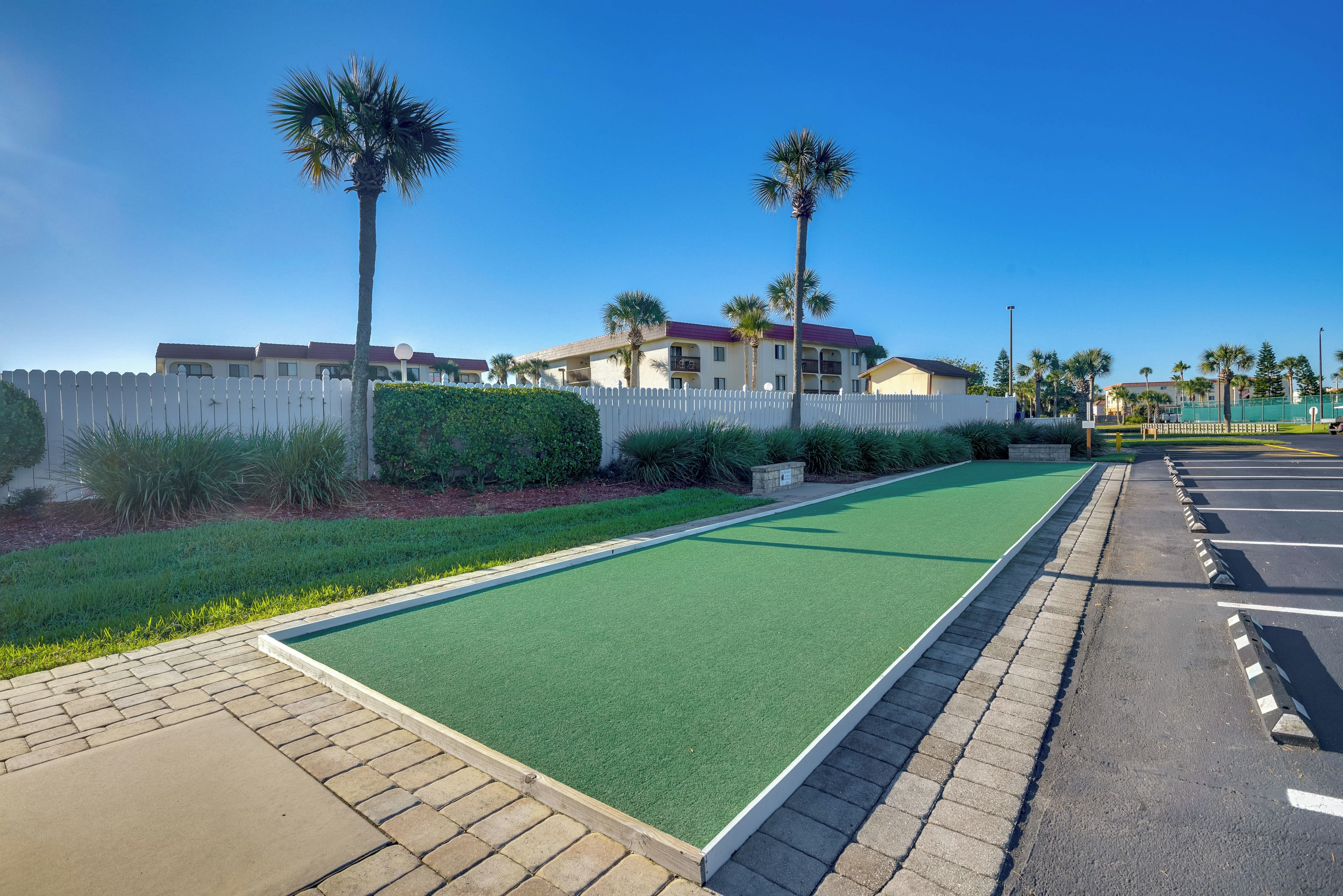 Een golfbaan met een groen fairway, een witte hekken en palmbomen.