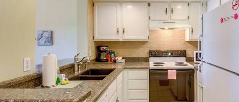 A compact kitchen with white cabinets, a granite countertop, a stove, and a refrigerator.