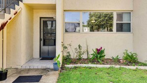 A two-story building with a front door, a small garden with plants and a flower bed, and a visible staircase to the upper floor. - Sunny Florida Condo: 4 Mi to Gulf Islands Seashore (Fort Walton Beach)