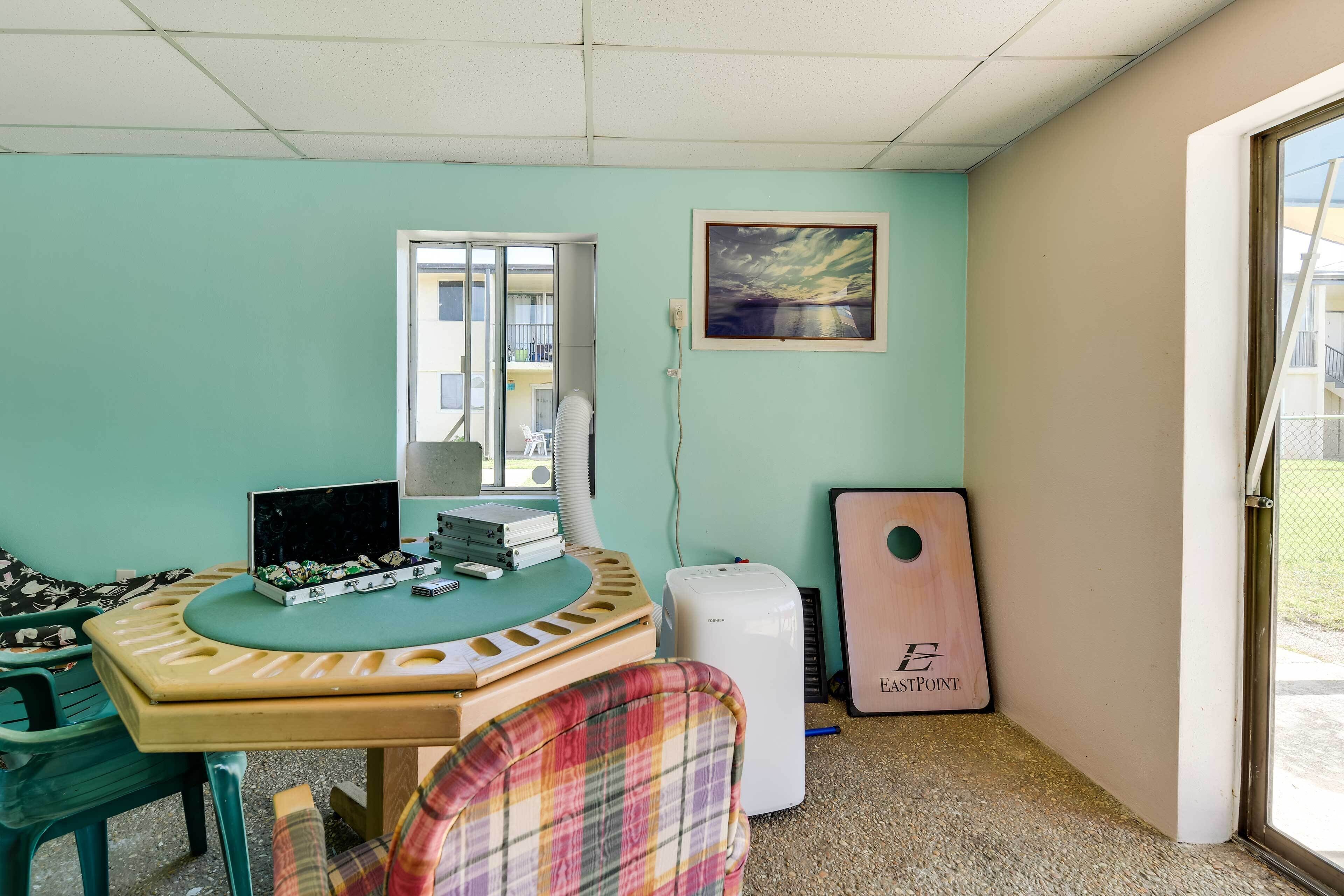 Una habitación con pared verde azulado, una ventana, un cuadro, un escritorio con una computadora, un pequeño enfriador de aire y una puerta con un panel de madera.
