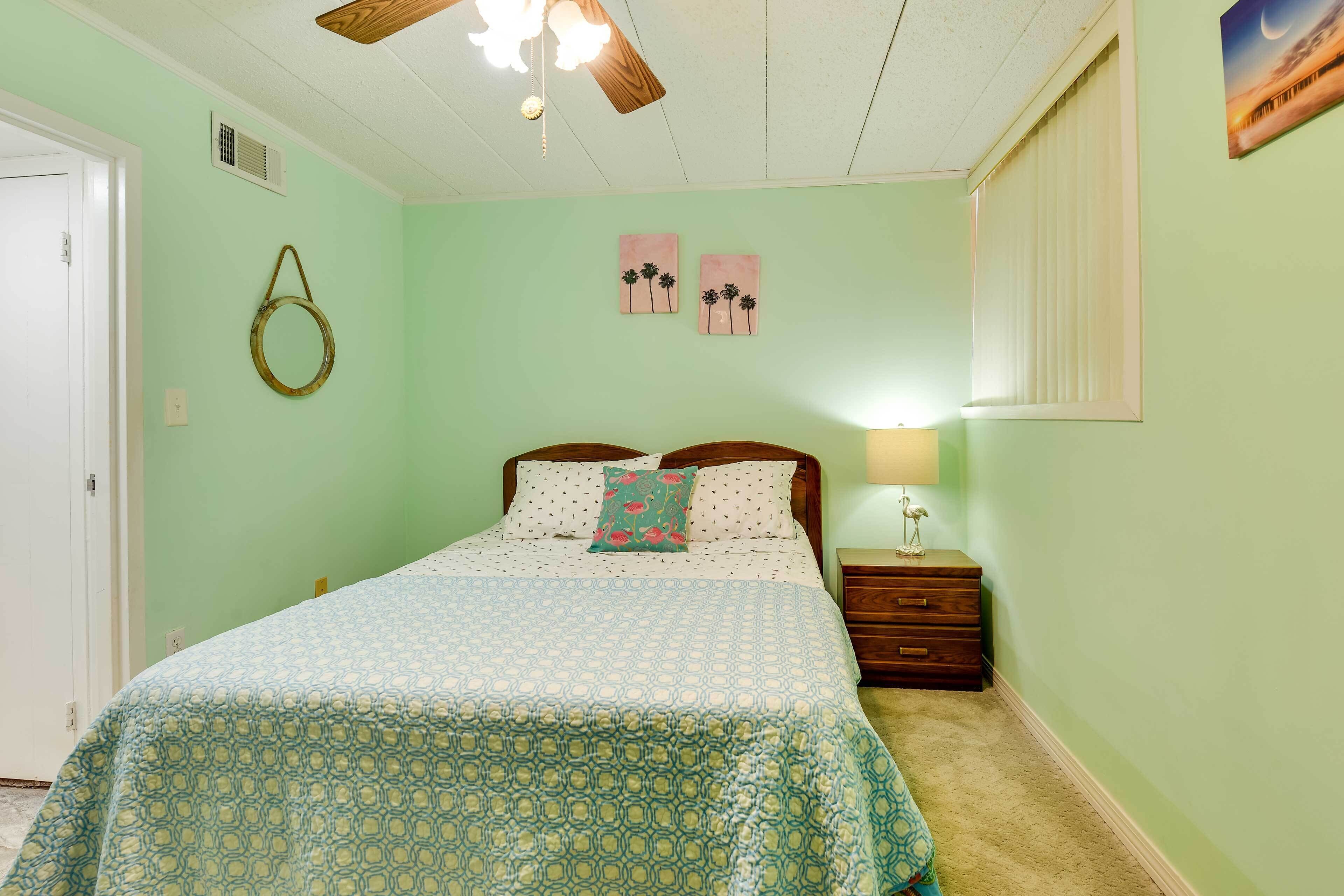 Un dormitorio con cama, mesita de noche, lámpara, ventilador de techo y decoración en la pared.