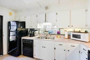 Una cocina con armarios blancos, un refrigerador negro, lavavajillas, microondas y un lavamanos.