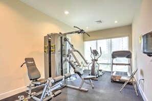 Uma academia com diversos equipamentos de exercícios, incluindo um banco de musculação, uma prensa de pernas e uma esteira.