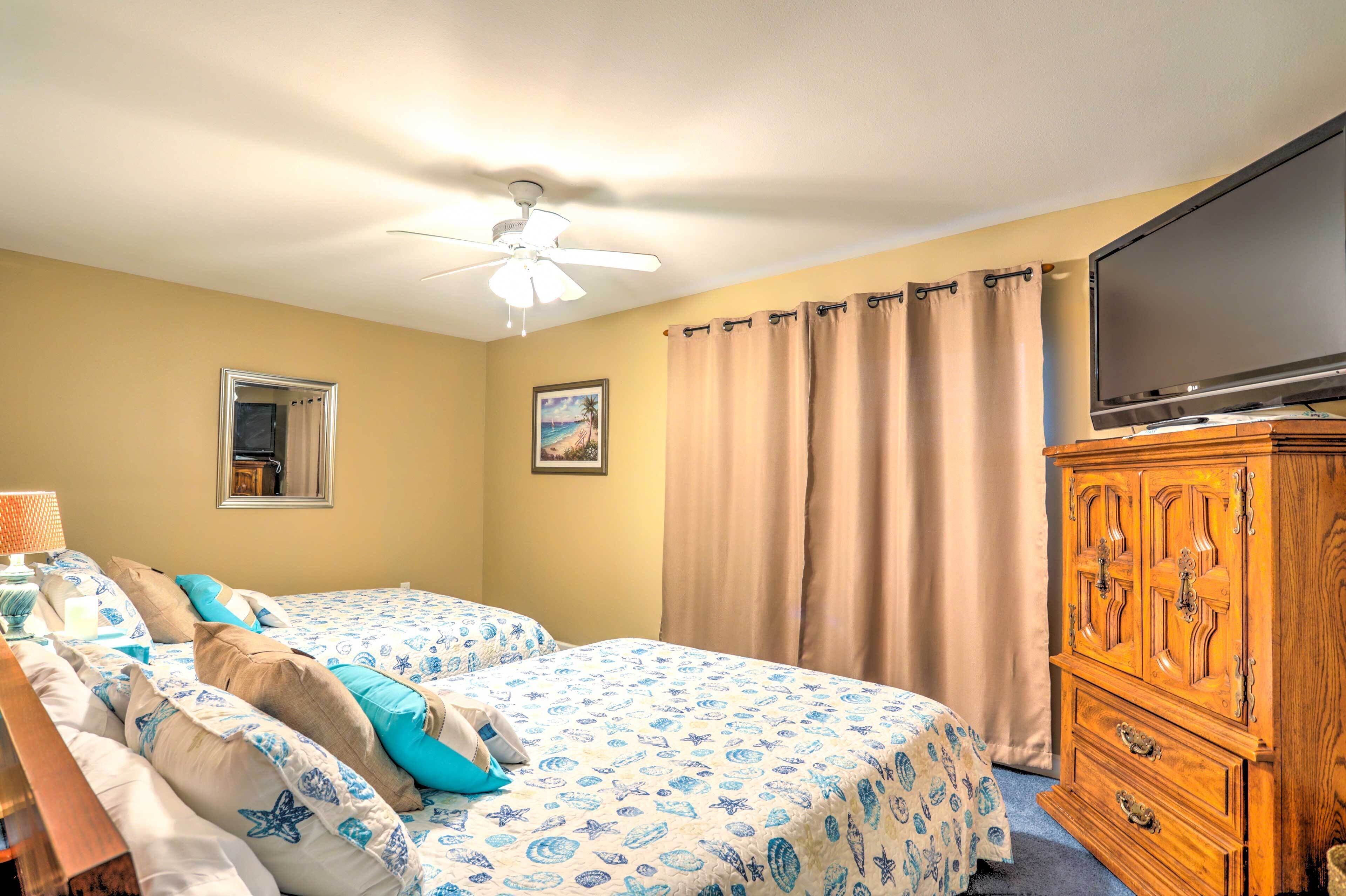 A hotel room with two beds, a ceiling fan, a television, a wooden dresser, and a window with curtains.