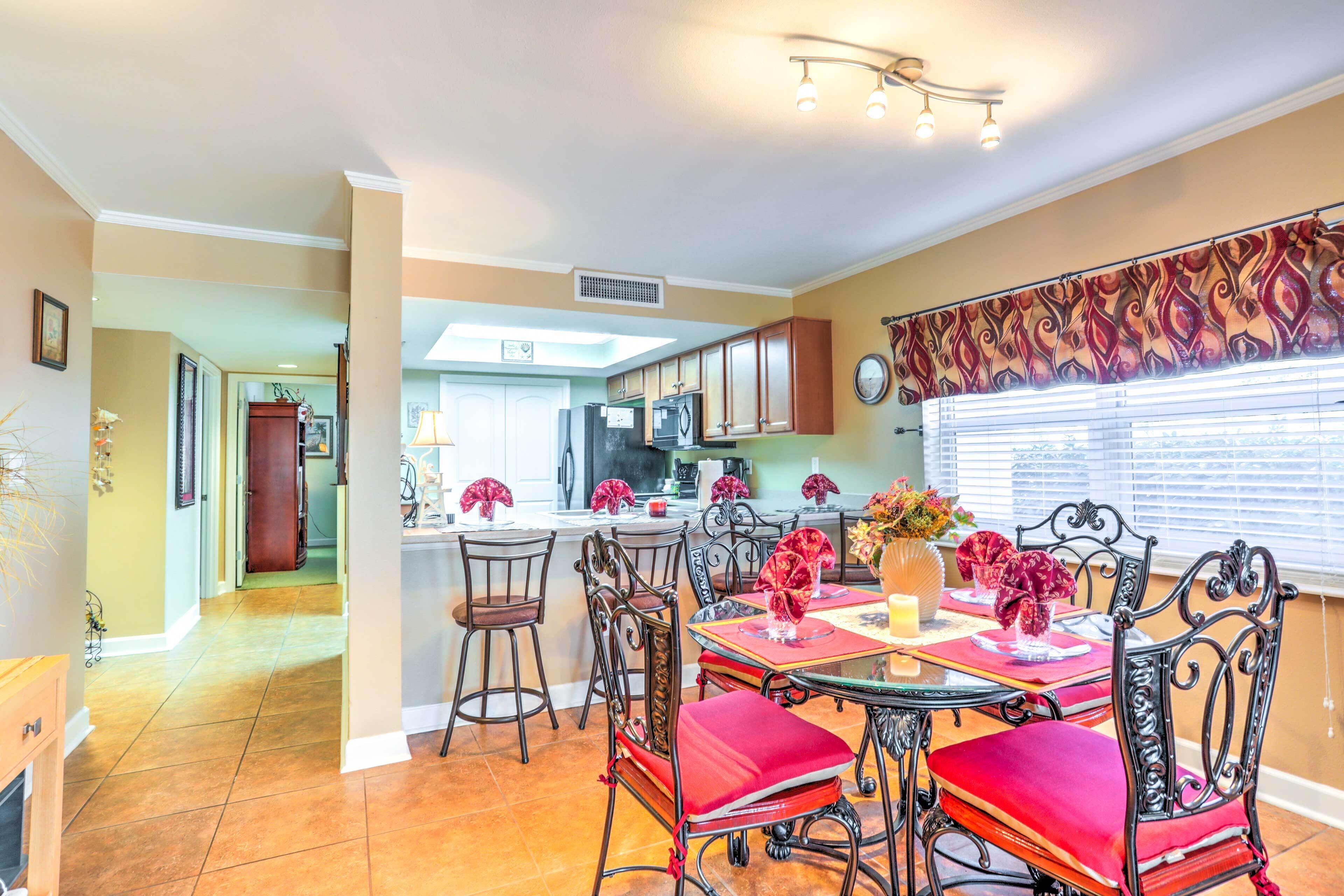 A dining area with a table set for four, surrounded by ornate chairs. A kitchen is visible in the background with modern appliances.
