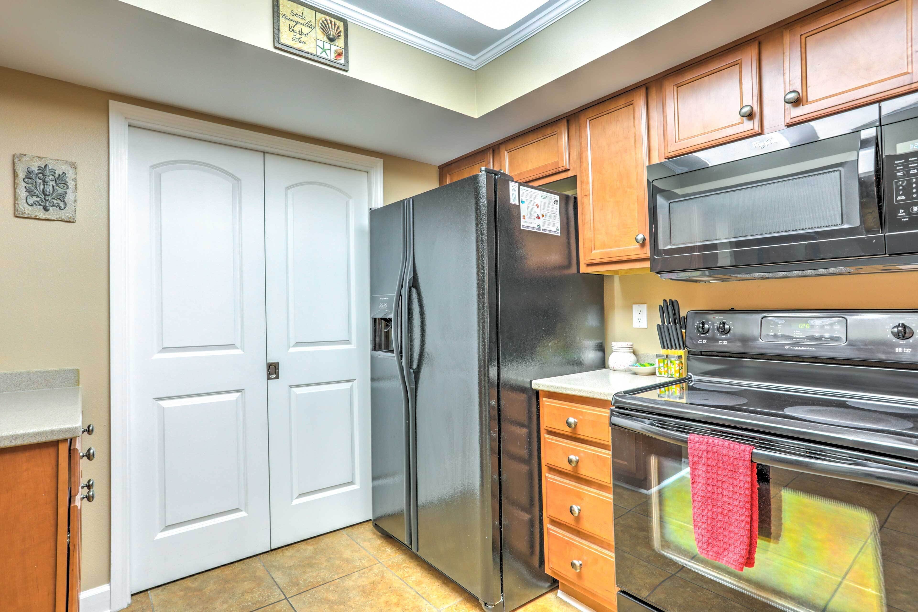 A kitchen with a stainless steel refrigerator, a microwave, and an oven. There is a white door and wooden cabinets.