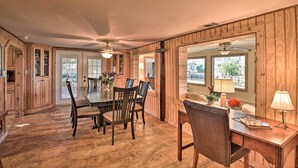 A spacious dining area with a wooden table and chairs, a ceiling fan, and a view of the outdoors through large windows. - St Johns River Canal Home w/ Grill! (Crescent City)