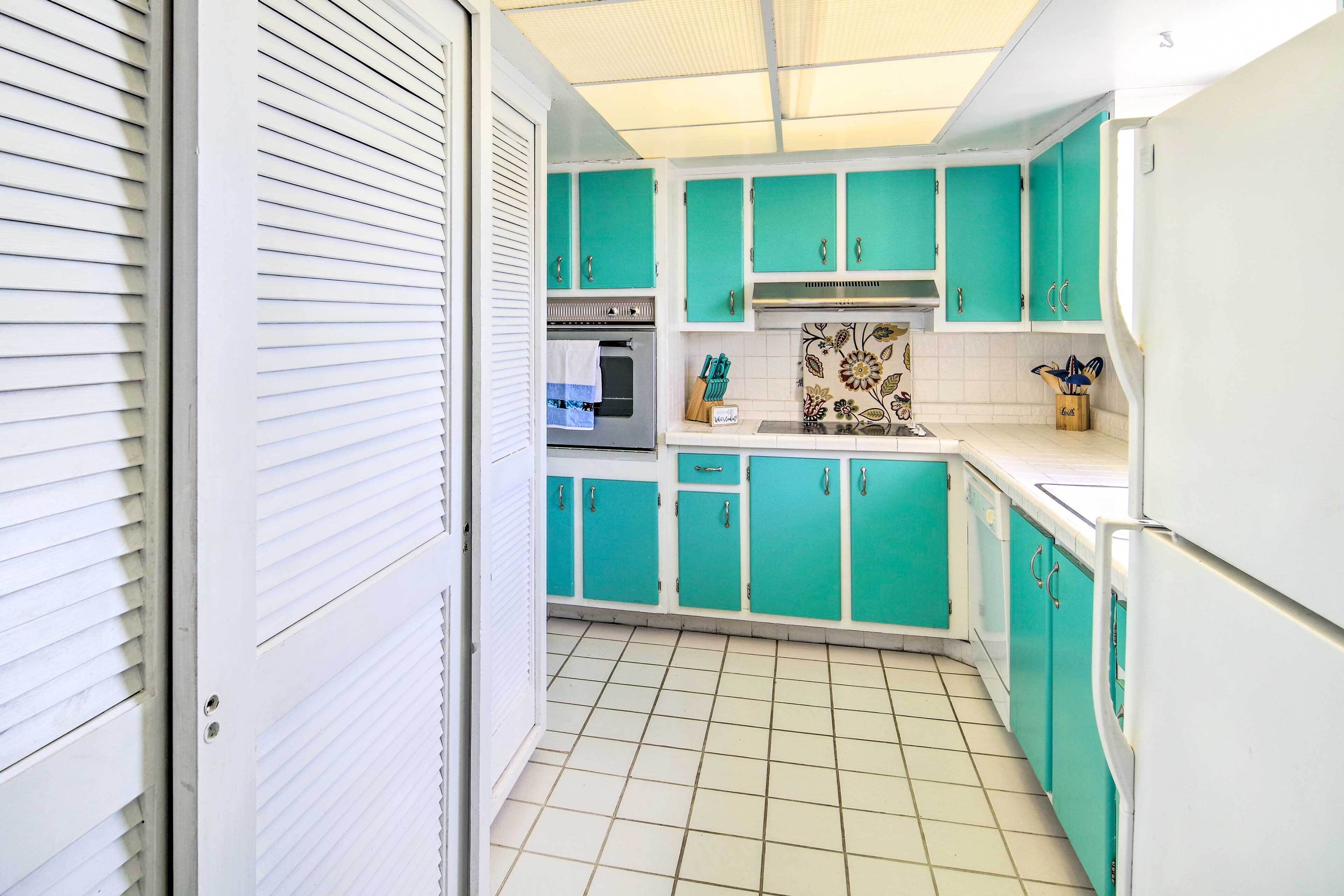 Una cocina con armarios color turquesa, un refrigerador blanco y suelo de baldosas.