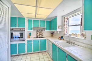 Una cocina con gabinetes azul turquesa, un horno de acero inoxidable y una ventana con cortinas decorativas.