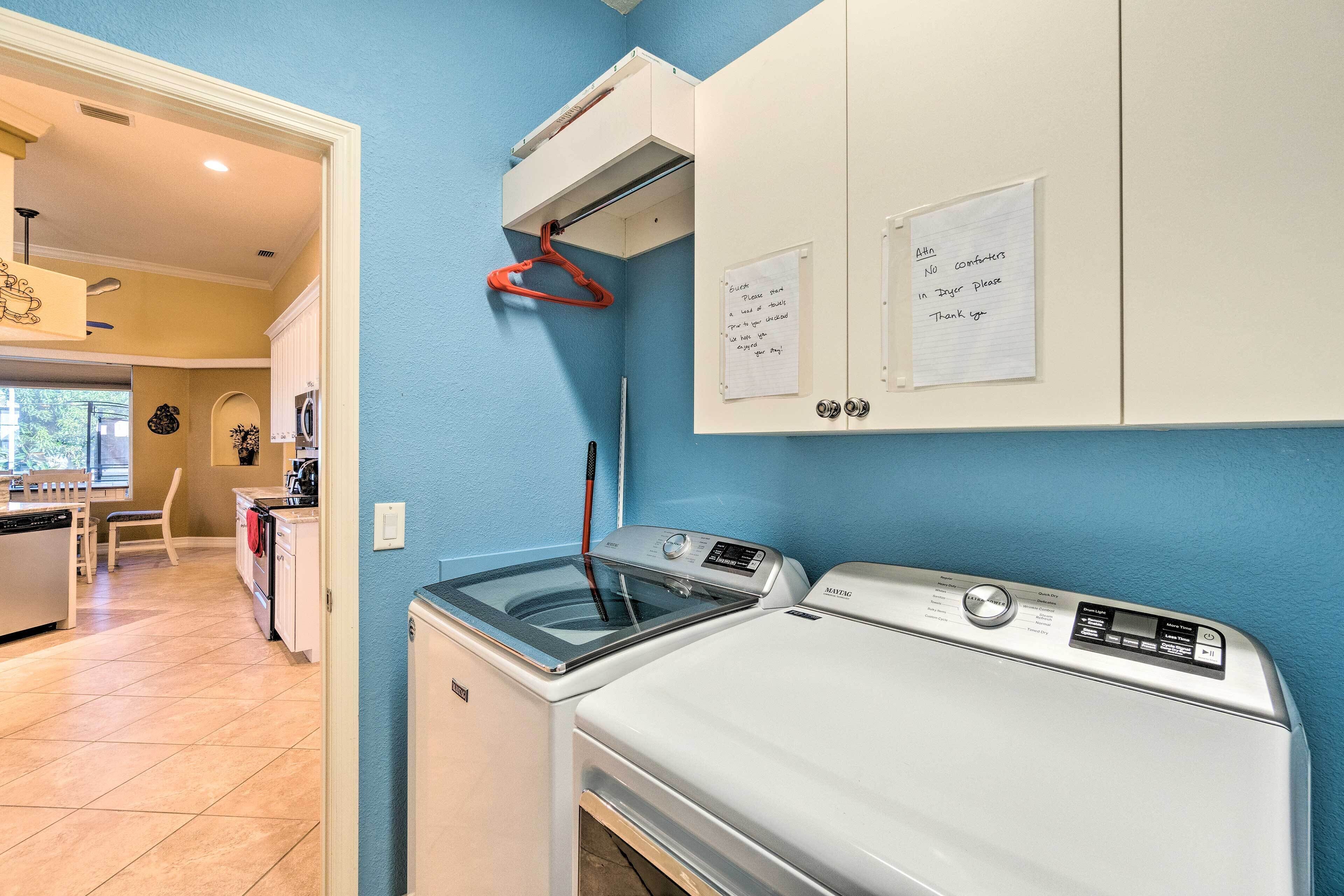 A laundry room with a front-loading washer and dryer, a drying rack, and a note on the wall.