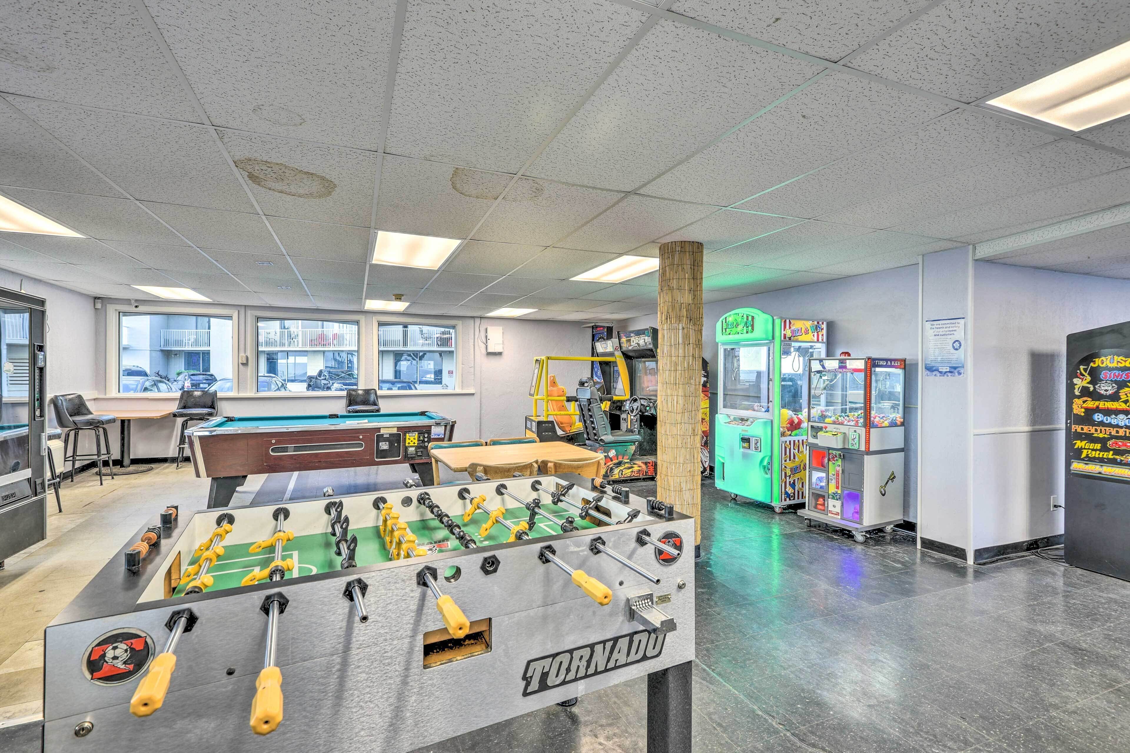 A room with a foosball table, pool table, and various arcade games.
