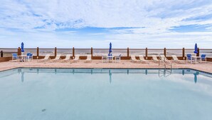 A pool with lounge chairs and umbrellas, a wooden fence, and a view of the beach. - Beachfront Studio w/ Community Indoor Pool! (Daytona Beach)
