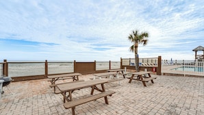 A beachside patio with picnic tables, a barbecue grill, and a pool area. - Beachfront Studio w/ Community Indoor Pool! (Daytona Beach)