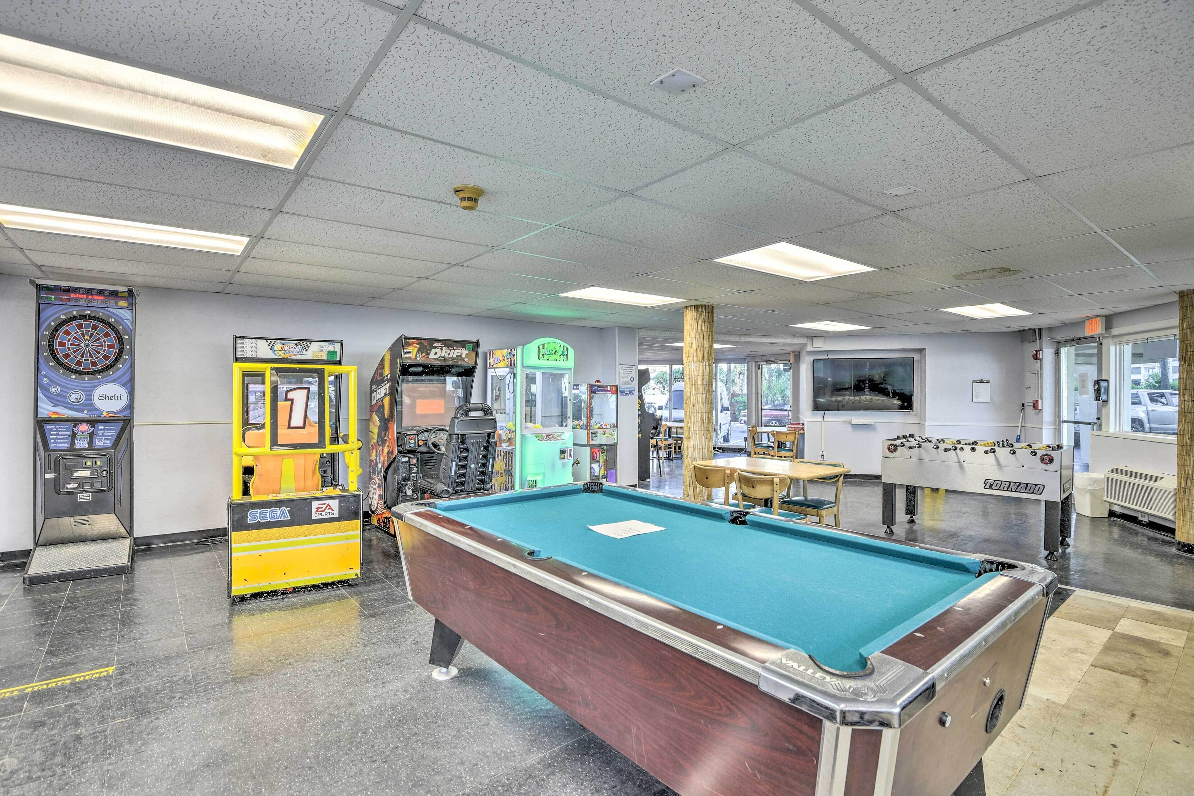 A pool table, arcade machines, and a foosball table in a recreational area.