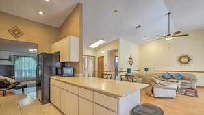 Une cuisine moderne dotée d’un îlot central, un coin repas avec un canapé et une table, et un salon avec un divan et des œuvres d’art décoratives au mur.
