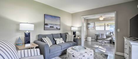 A living room with a grey sofa, striped armchair, and ottoman, a painting on the wall, and a desk in the background.