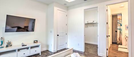A modern bedroom with a bed, a TV, a white console, and a hallway leading to a bathroom.