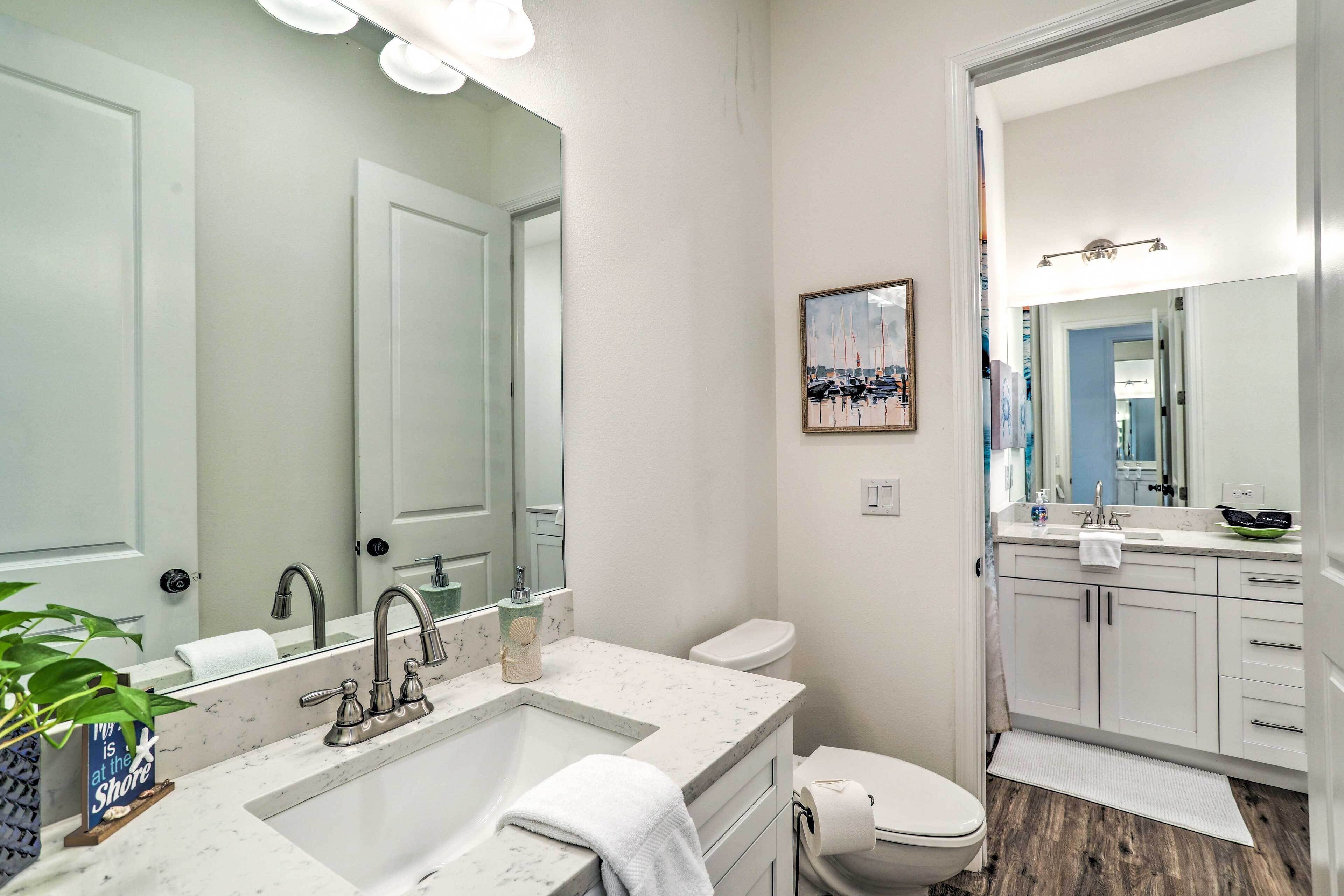 Une salle de bain moderne avec un grand miroir, un lavabo doté d’un plan de travail en marbre, des toilettes et un espace douche.