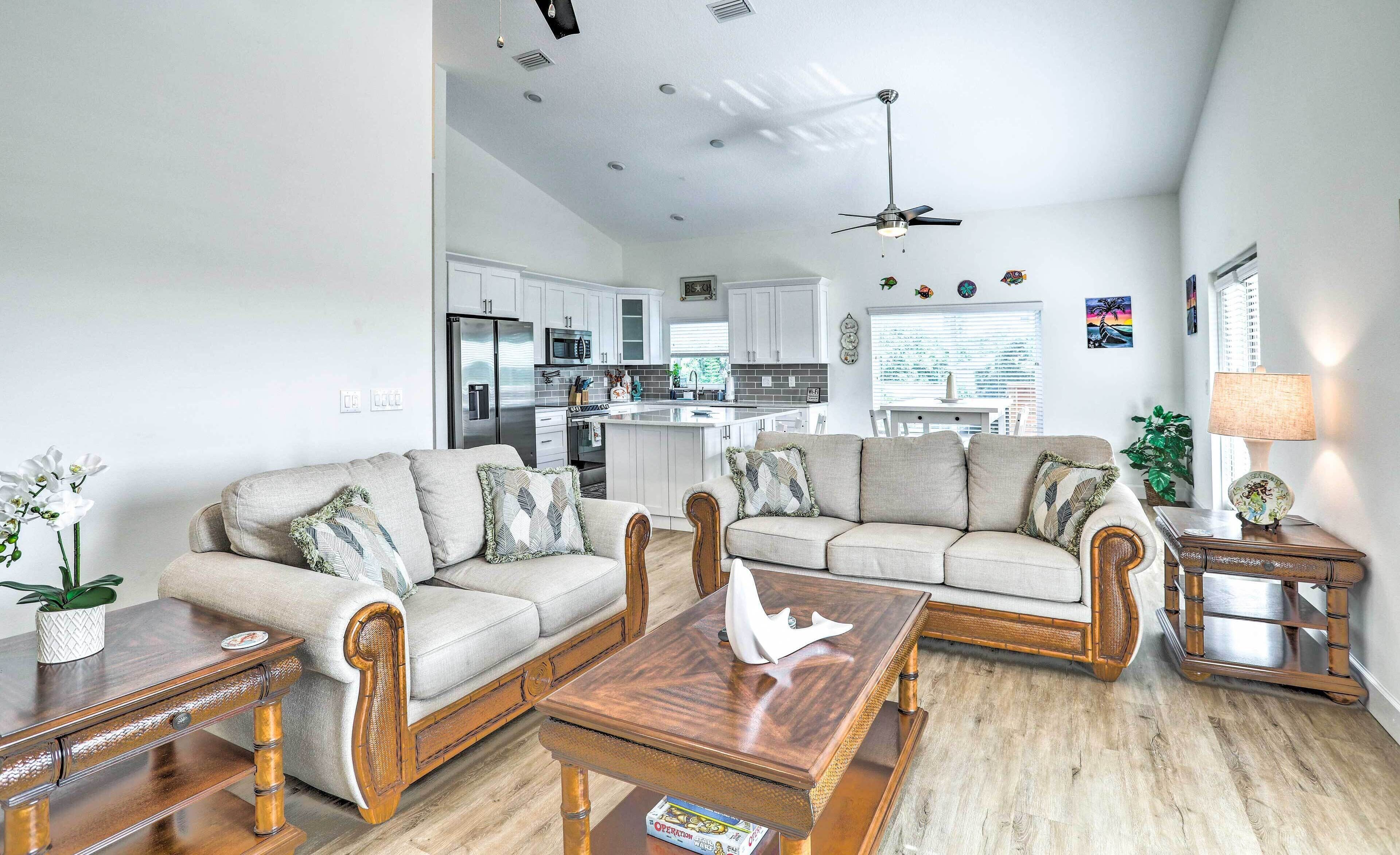 A spacious living room with a sofa set, wooden coffee table, and a dining table. A kitchen with modern appliances and a dining area with a lamp are visible in the background.