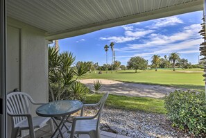 A covered patio with a table and chairs, overlooking a golf course with palm trees and a clear sky. - St Pete Condo w/ Heated Pool - 3 Miles to Beach! (St. Petersburg)