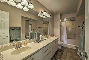 A bathroom with a large mirror, two sinks, a shower, and a toilet.
