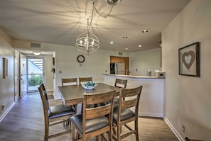 A dining area with a wooden table and chairs, a chandelier, and a kitchen in the background. - St Pete Condo w/ Heated Pool - 3 Miles to Beach! (St. Petersburg)