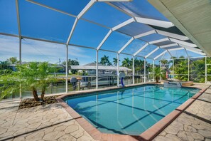 A swimming pool with a glass enclosure, palm trees, and a view of a water body and buildings in the background. - 3 Mi to Downtown Cape Coral: Canal-front Villa (Cape Coral)