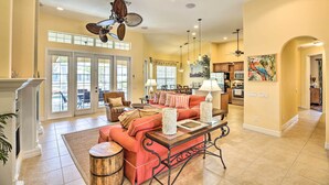 A spacious living room with a fireplace, a ceiling fan, and a large window overlooking a patio. - 3 Mi to Downtown Cape Coral: Canal-front Villa (Cape Coral)