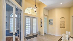 A spacious hallway with a high ceiling, a chandelier, and a dining area with a glass table. - 3 Mi to Downtown Cape Coral: Canal-front Villa (Cape Coral)
