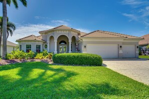 A two-story house with a tiled roof, a garage, and a well-maintained lawn. - 3 Mi to Downtown Cape Coral: Canal-front Villa (Cape Coral)