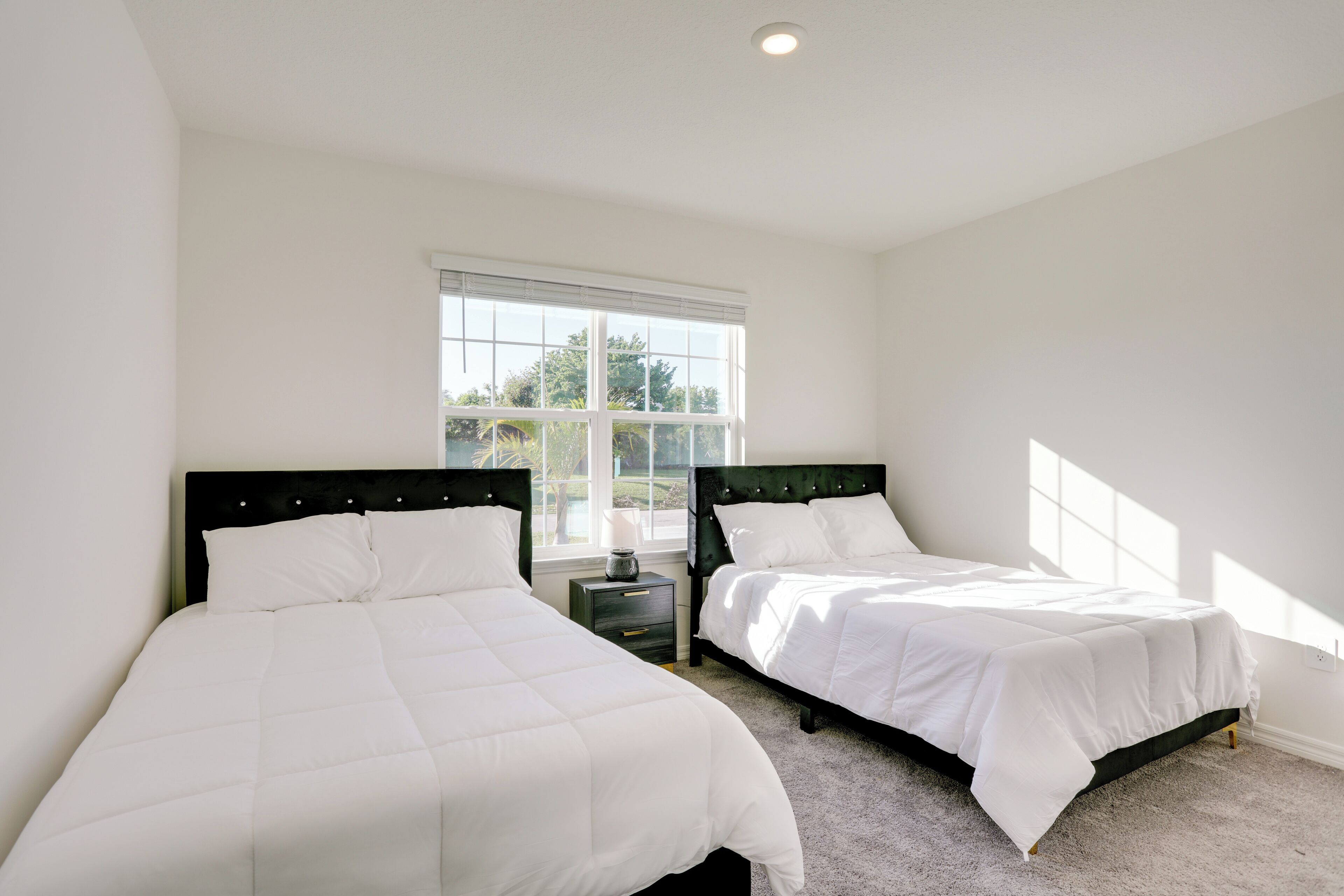A bedroom with two beds, a window, and a nightstand.