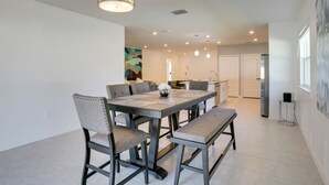 Uma sala de jantar com uma mesa retangular, seis cadeiras e um banco. Há luminárias pendentes sobre a mesa.