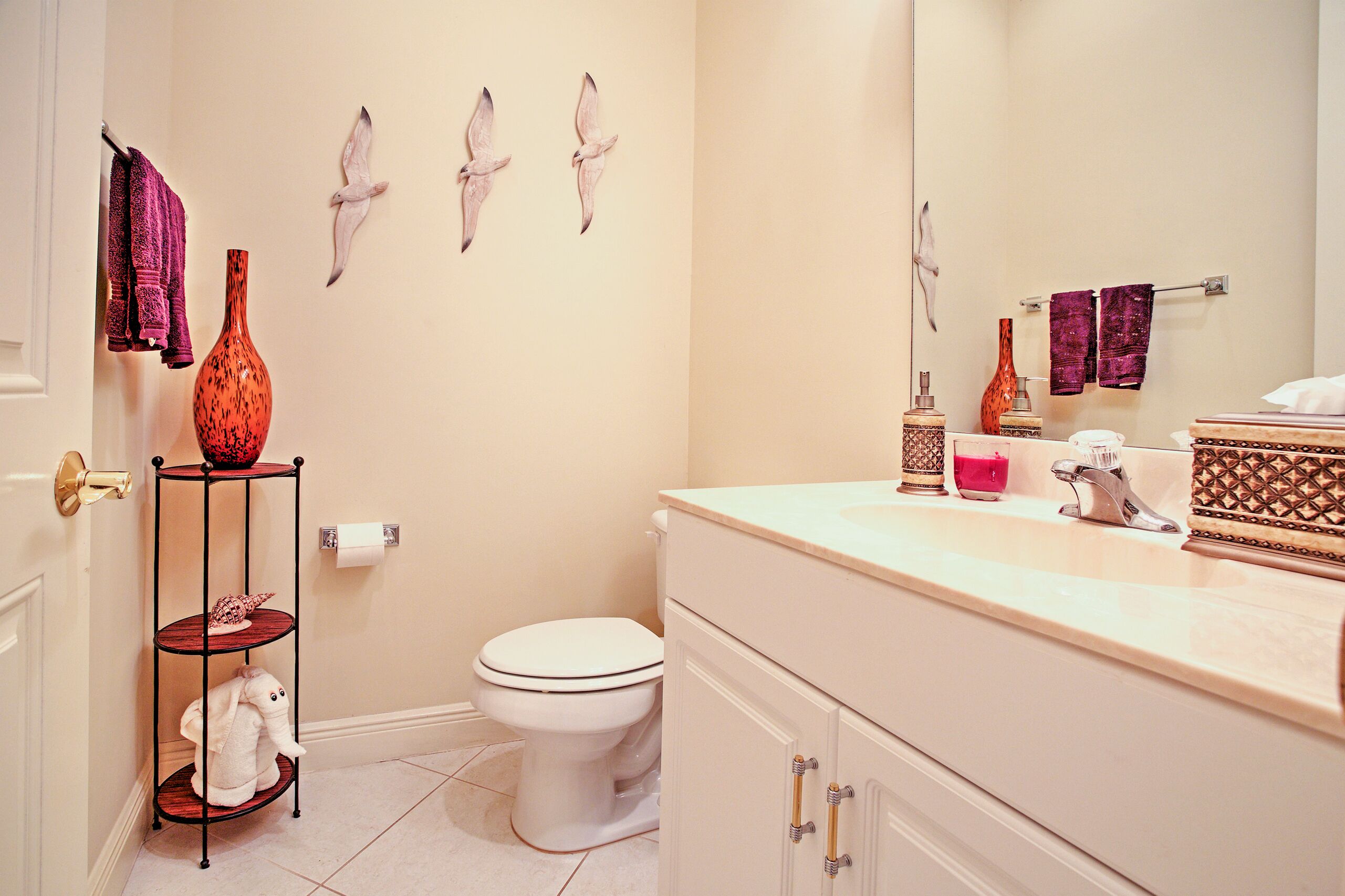 A bathroom with a toilet, sink, vanity, and decorative items like towels and a vase.