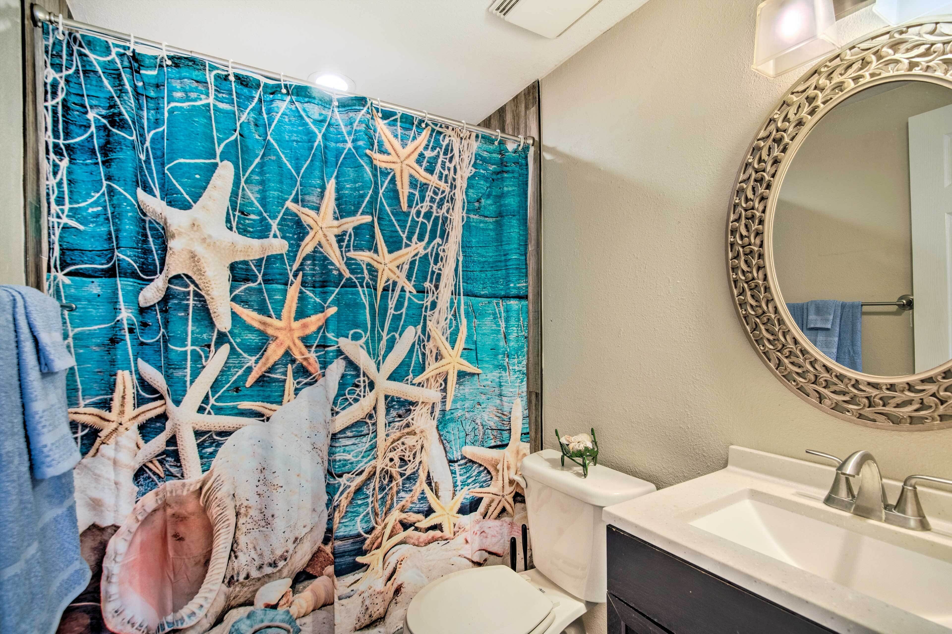 A bathroom with a blue curtain featuring starfish and seashells, a white sink, and a mirror with an ornate frame.