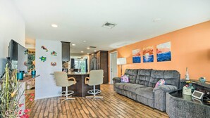 A living room with a grey sofa, two chairs, a coffee table, and a TV. There are decorative wall art pieces and a wooden floor.