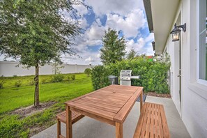 Um pátio externo com uma mesa e um banco de madeira, uma churrasqueira e uma árvore.